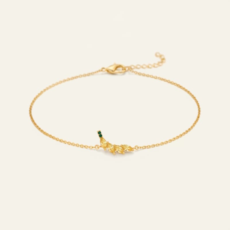 Gold bracelet with 2 green gemstones for the stem and 4 yellow stones on a light beige background representing a banana