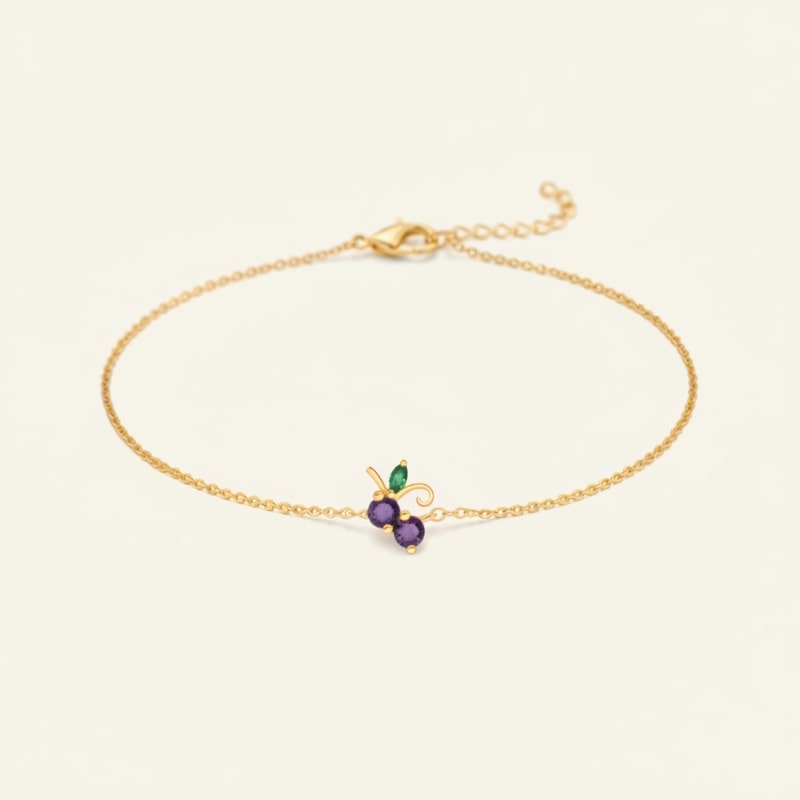 Gold bracelet with a purple gemstone and green leaf on a beige background