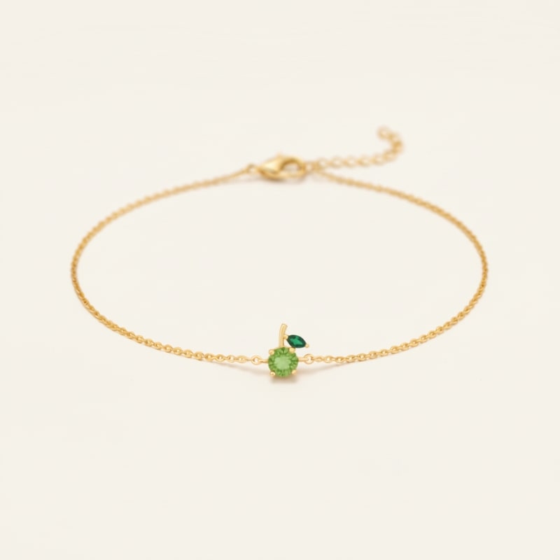 Gold bracelet with a 2 green gemstones on a light beige background representing a green apple