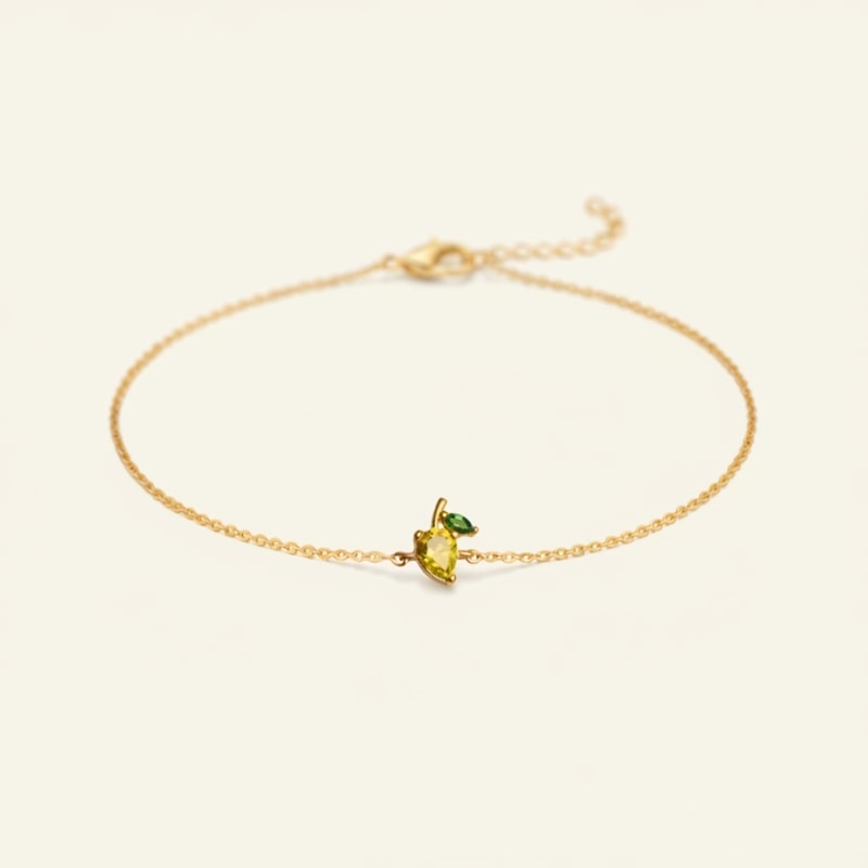 Gold bracelet with a yellow and green gemstones on a beige background representing a mango