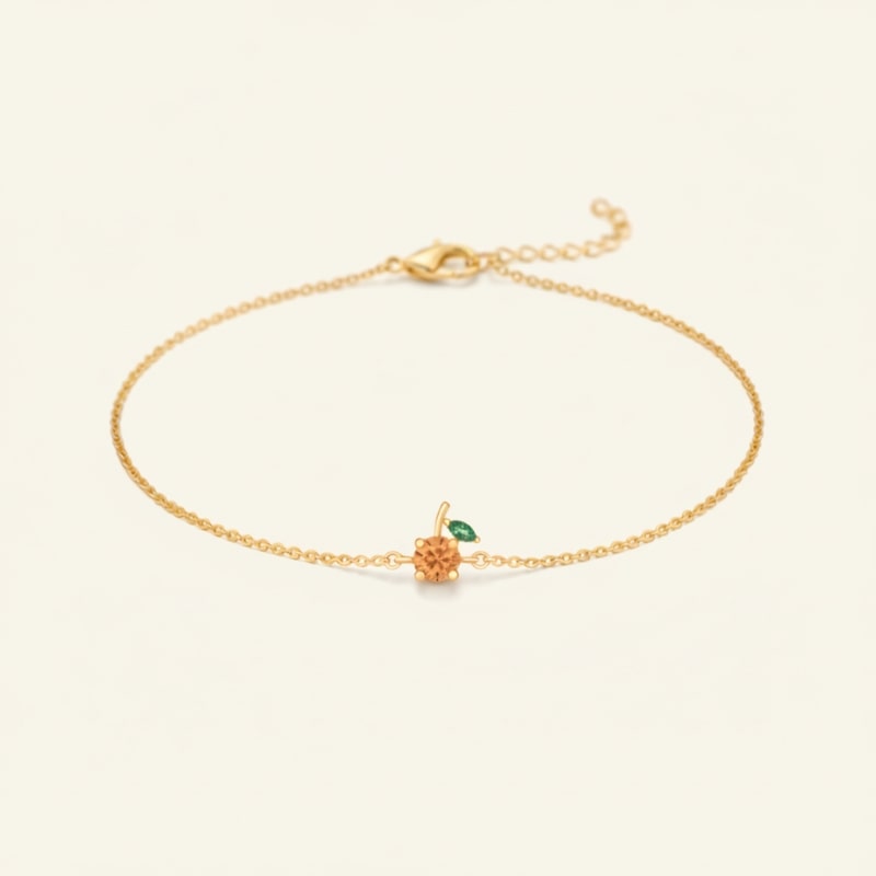 Gold bracelet with a small orange and green gemstones on a light beige background